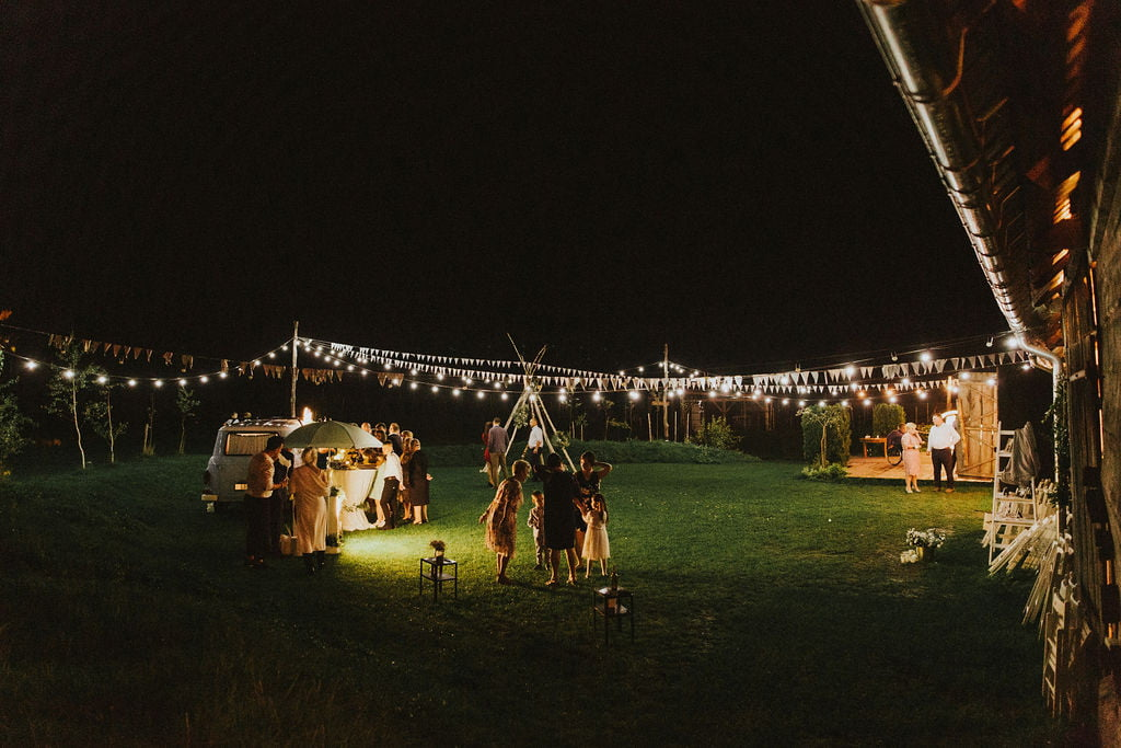 Event plenerowy w stylu rustykalnym - drewniane stoły, dekoracje wiejskie i goście biesiadujący na świeżym powietrzu